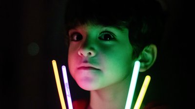 A boy playing with a glow stick in lowlight conditions