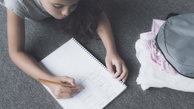 A girl lies on the floor next to her backpack and draws a pencil in a white notebook escape plan