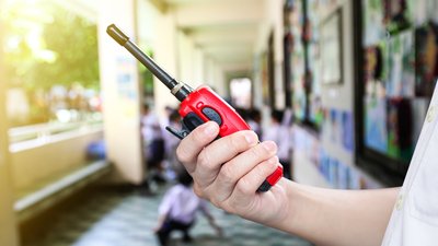 A man holding a red radio communication or handheld walkie-talkie at school