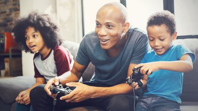 African American family at home sitting in sofa couch and playing console video games together
