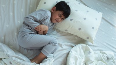 Asian boy lying in bed with stomach ache