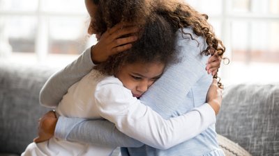 Black African mother embrace little preschool frustrated kid sitting on couch together at home