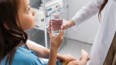 Doctor giving glass of water to child on hospital bed