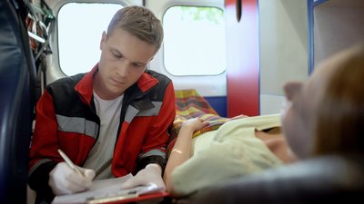 EMT filling out medical form in ambulance, emergency help to female patient