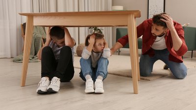 Father comforting his scared children under table in living room during earthquake