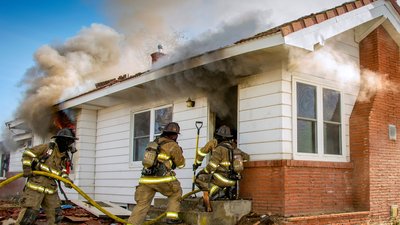 Fire fighters in full breathing apparatus enter a smoke filled house on fire