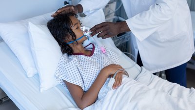 Midsection of male doctor putting oxygen mask ventilator on sick mixed race girl in hospital bed