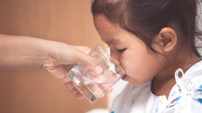 Mother hand giving glass of water to sick child girl in the hospital