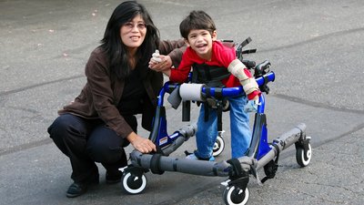 Mother helping disabled son walk in walker outdoors