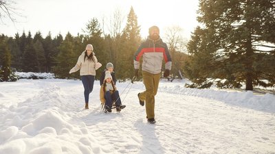 Parents take children on sleds while happily walking along snowy path in winter park