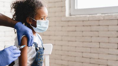 Pediatrician injecting vaccine to little african girl in medical clinic