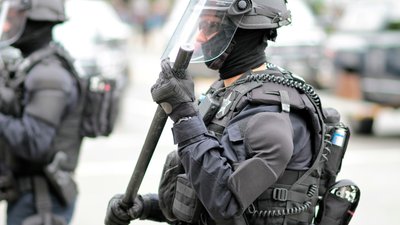 Police officer in riot gear overseeing a crowd of protestors