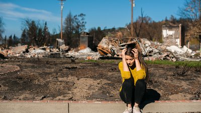 Sad woman home owner holds his head by hand checking burnt out house and yard after fire disaster, consequences of fire disaster accident