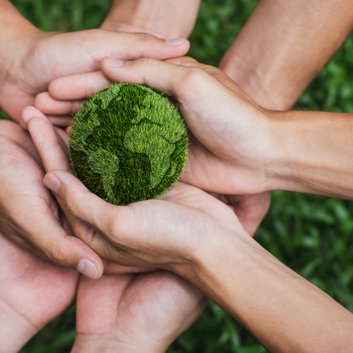 Several hands holding a grassy green earth ball