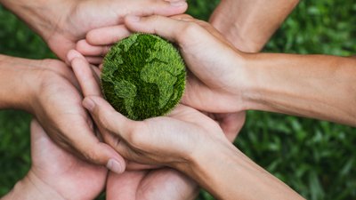 Several hands holding a grassy green earth ball