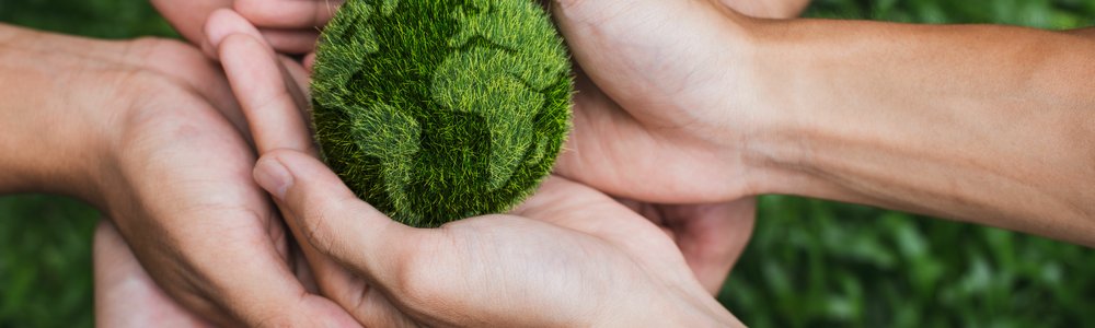 Several hands holding a grassy green earth ball