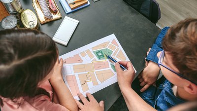 Top view of unrecognizable mother explaining to her children the assembly point map while preparing emergency backpacks