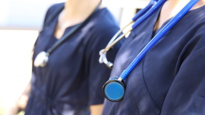 Two female medical practicioners in blue uniform with stethoscopes around their necks