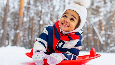 Winter portrait of happy little girl wearing knitted hat and a jumpsuit outdoor in winter