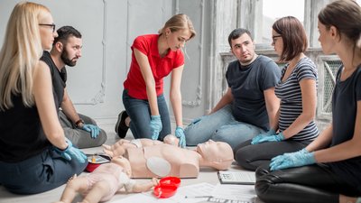 Woman instructor showing how to make chest compressions on a baby dummy during the first aid group training indoors