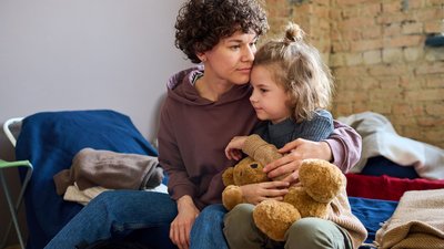 Young woman giving hug to her cute little son with brown soft teddybear