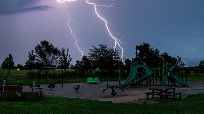 electrical lighting streaks across the sky during thunderstorm moving over children's playground